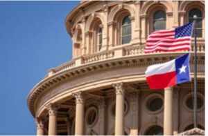 Two texas flags flying in front of the capitol building.